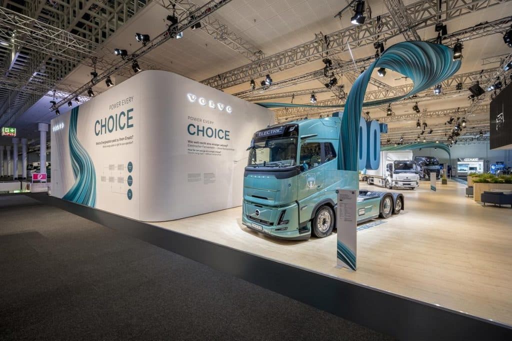 Volvo-Trucks-Messestand auf der IAA Transportation 2026: Ein türkisfarbener Lkw steht unter einer blaugrünen, geschwungenen textilen Deckenkonstruktion.